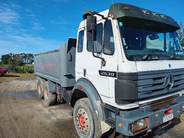 White Mercedes dump truck parked on a dirt lot under a blue sky