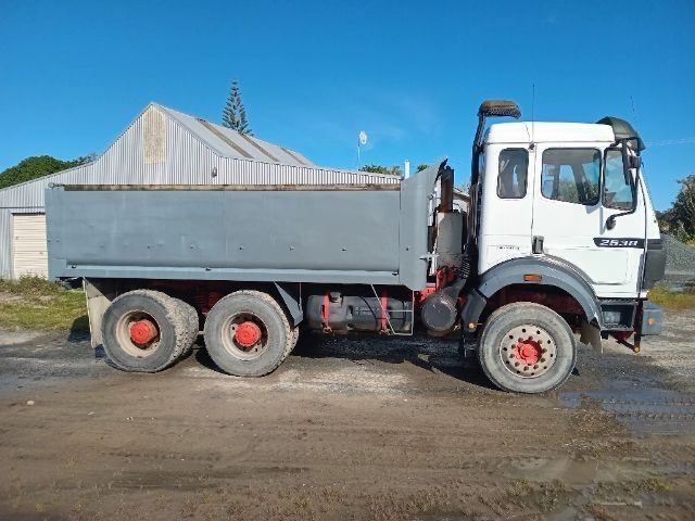 White dump truck parked on a muddy lot beside a metal-roofed building