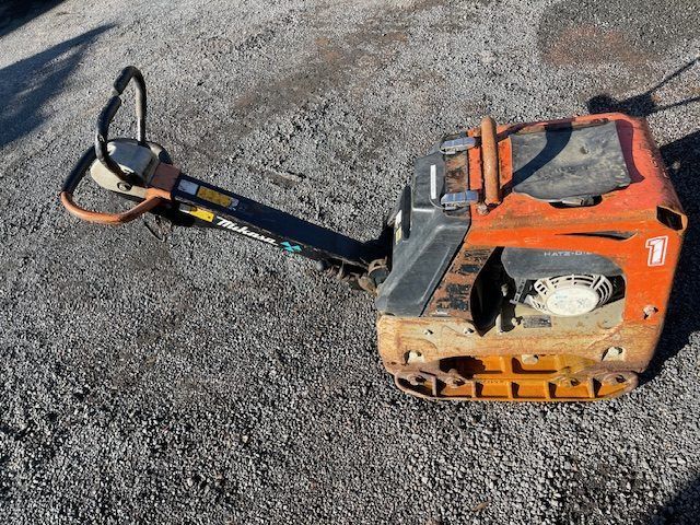 An orange and black machine is sitting on a gravel road.