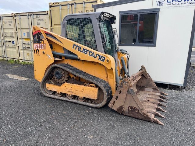 A mustang bulldozer is parked in front of a building.