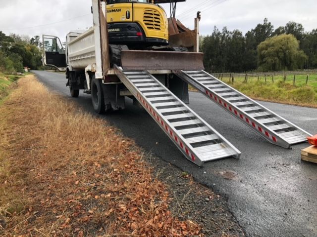 A yellow excavator is being loaded onto a dump truck with ramps.
