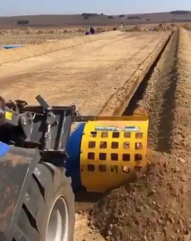 A yellow and blue tractor is plowing a dirt field.