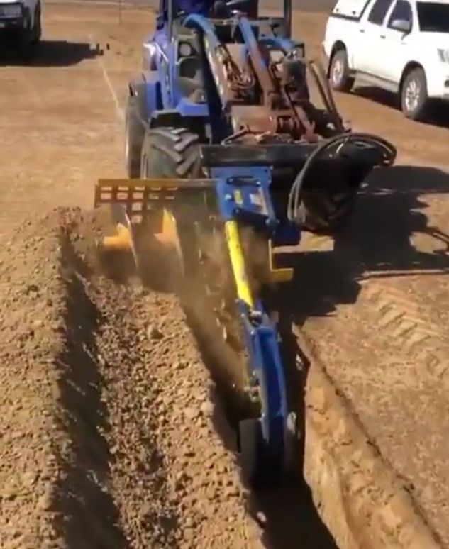 A blue and yellow tractor is digging a trench in the dirt.
