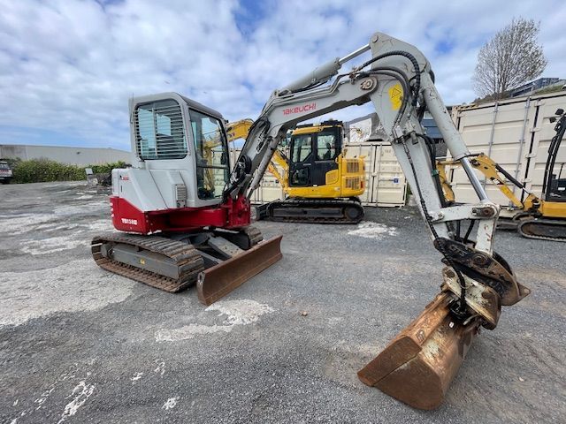 Two excavators parked on gravel, one white-red and one yellow, with buckets raised in a work yard.