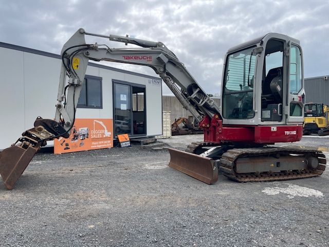 Red excavator parked outside a small industrial building on gravel lot