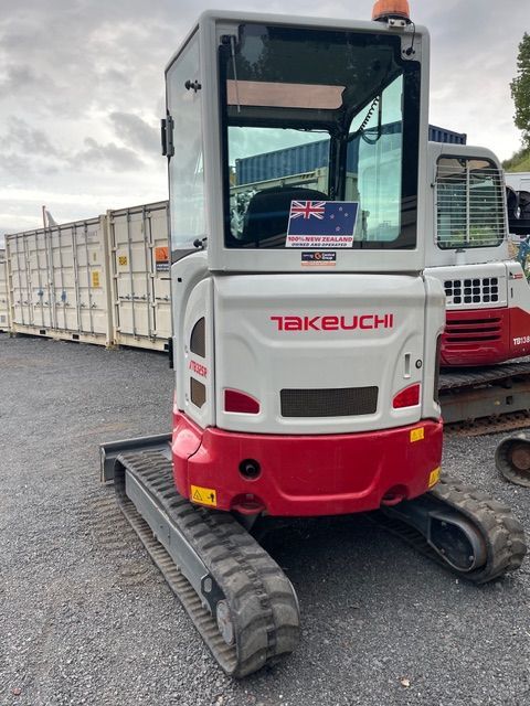 Takeuchi mini excavator with white cab and red base parked on a lot with shipping containers