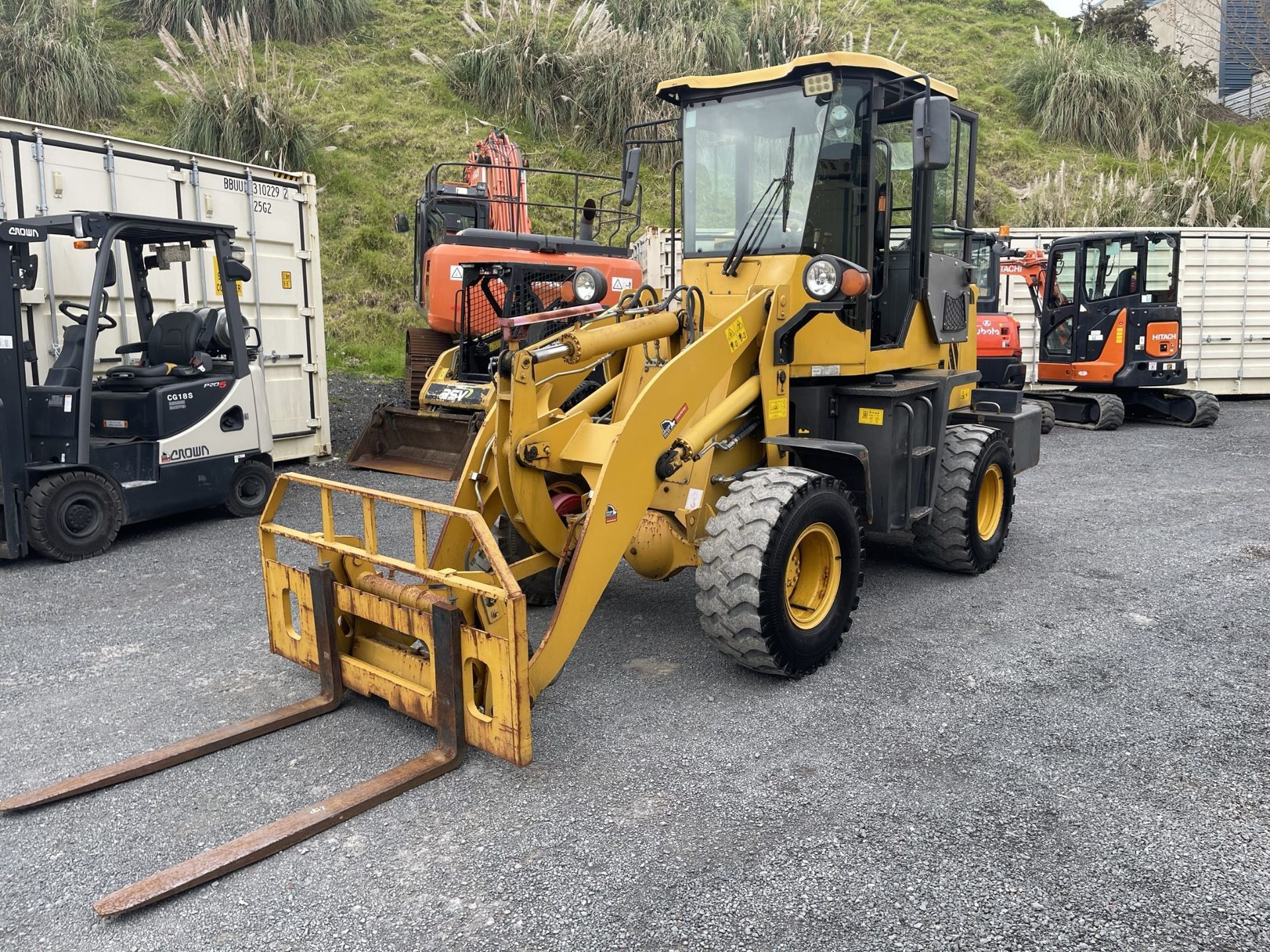 A yellow wheel loader with forks is parked in a gravel lot.