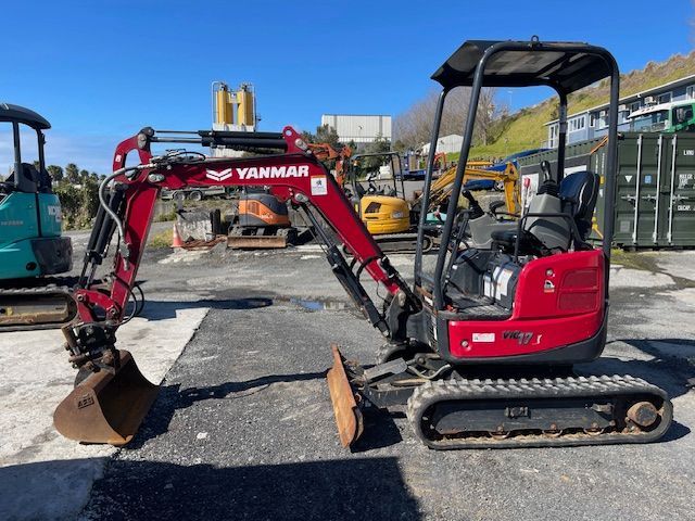 Red mini excavator with bucket raised on a construction site under a clear blue sky