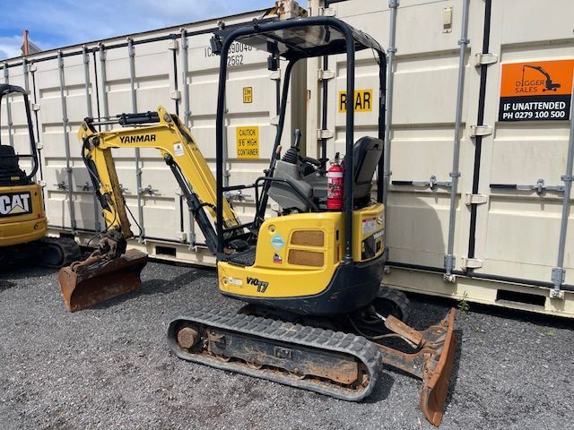 Yellow CAT mini excavator with tracks and bucket parked beside a white storage container.