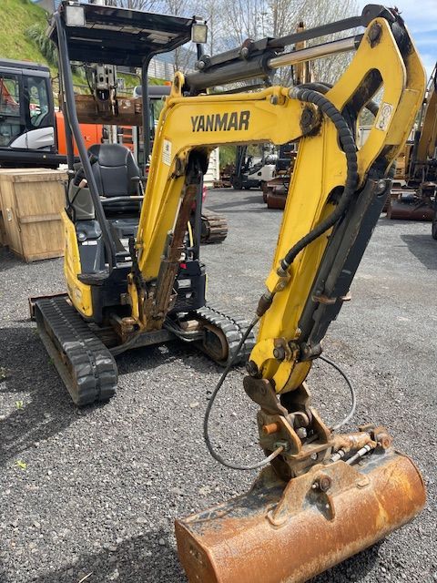 Yellow Yanmar mini excavator with bucket, parked on gravel at a construction yard
