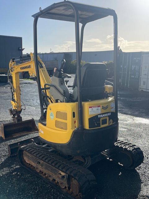 A small yellow excavator is parked in a parking lot