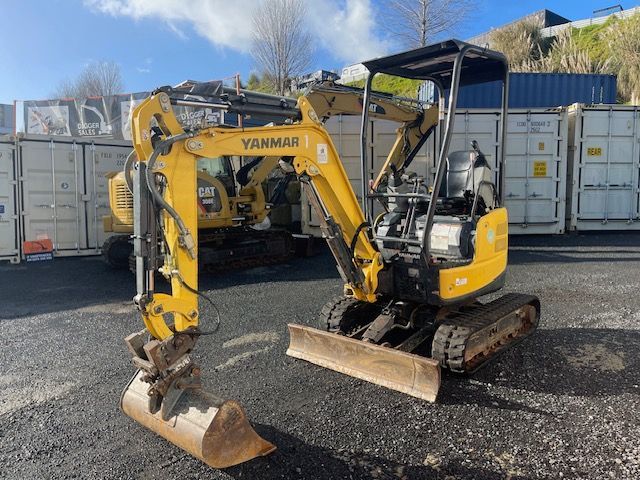 A small yellow excavator is parked in a parking lot.