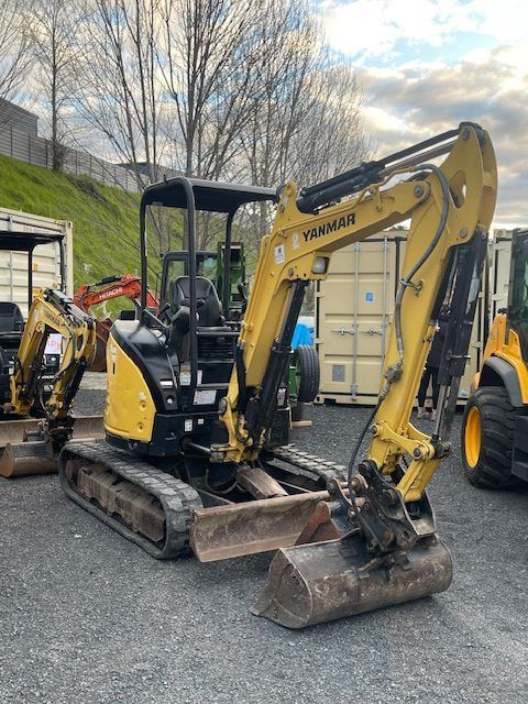 A small yellow excavator is parked in a parking lot.