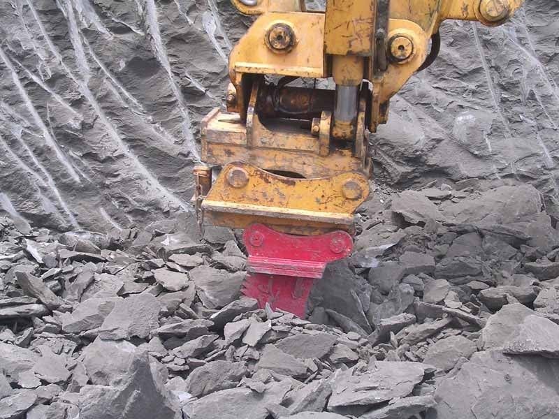 A yellow excavator is breaking up a pile of rocks.