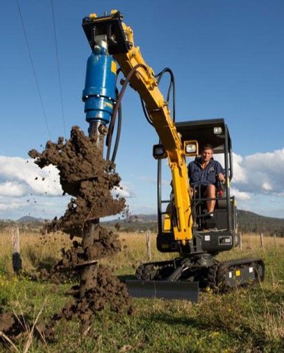 A man is driving a yellow excavator in a field.