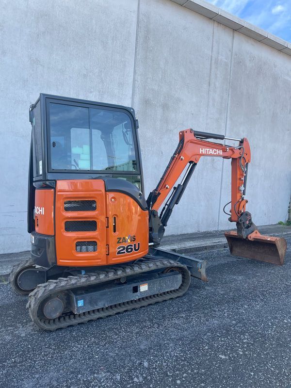 A small orange excavator is parked in front of a building.