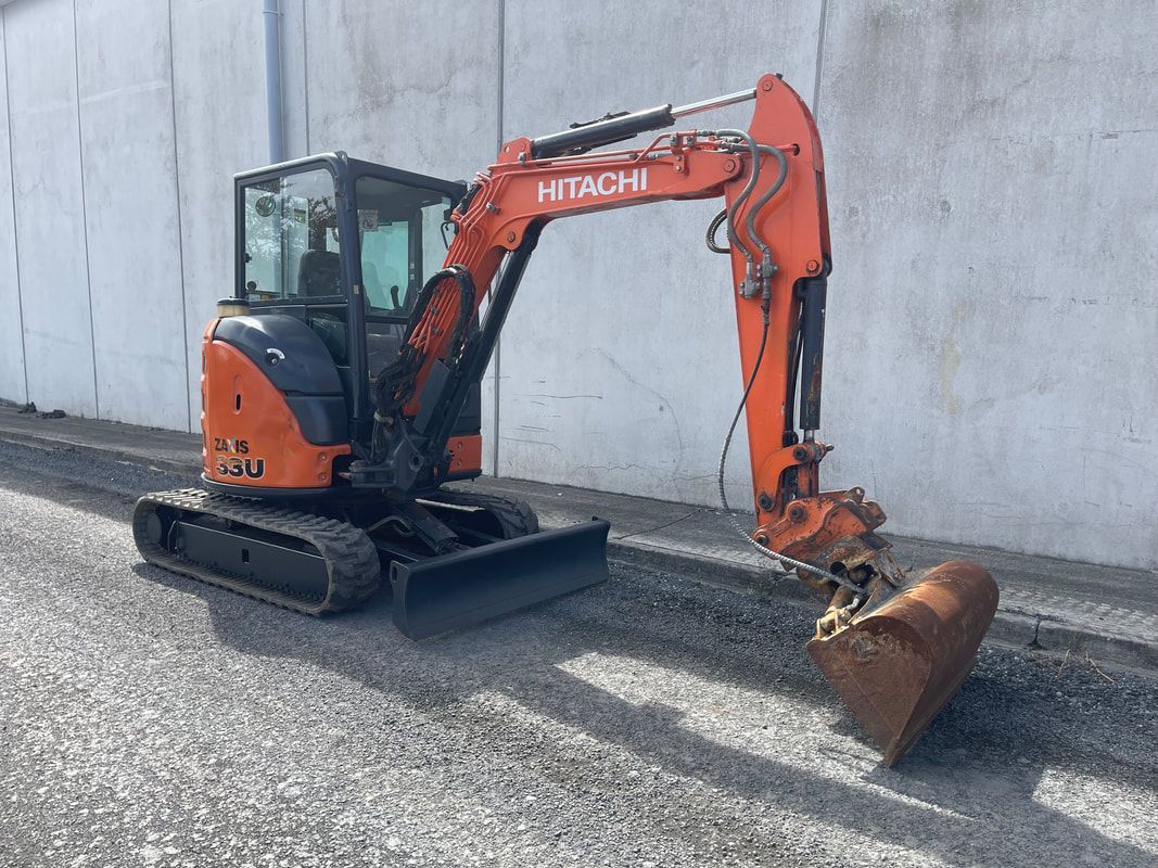 A small orange excavator is parked in front of a building.