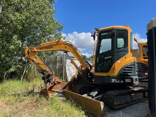 A yellow and black excavator is parked in a grassy field.