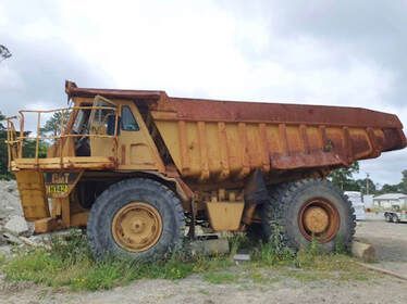 A large yellow dump truck is parked in a dirt lot.