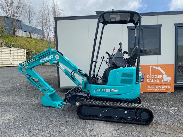 A small blue excavator is parked in front of a building.
