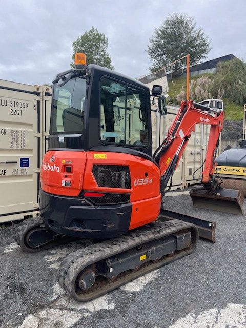 A small red and black excavator is parked in front of a shipping container.