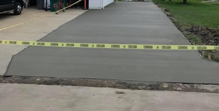 Concrete driveway blocked by yellow caution tape across a wide freshly poured slab