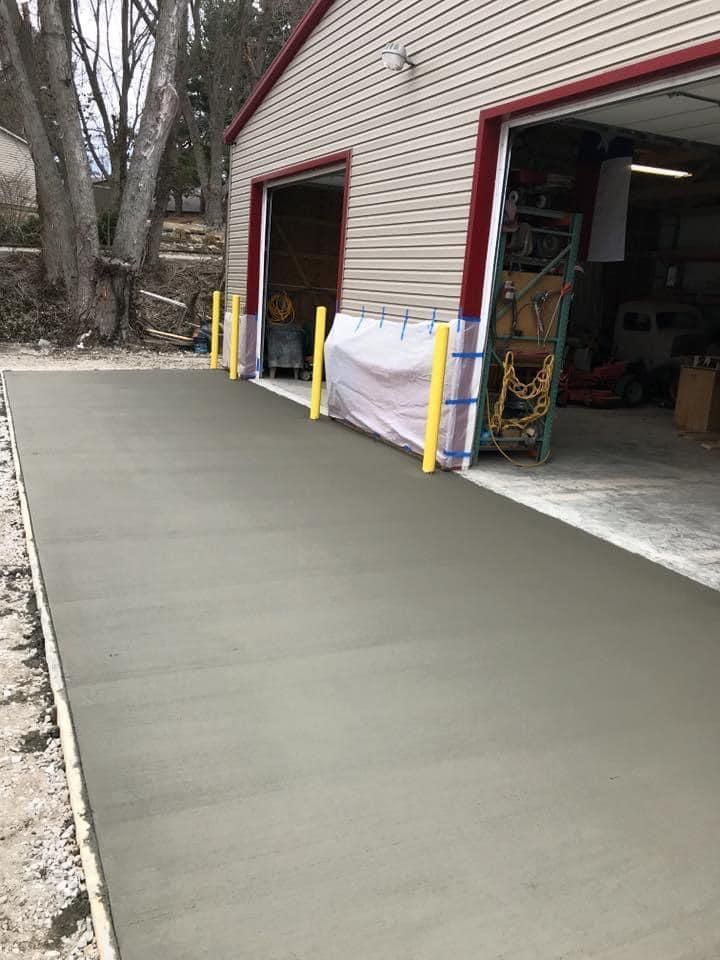 Freshly poured concrete driveway ramp beside a garage, with yellow posts and a covered opening.
