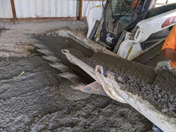 Skid-steer loader pouring wet concrete onto a floor inside a warehouse