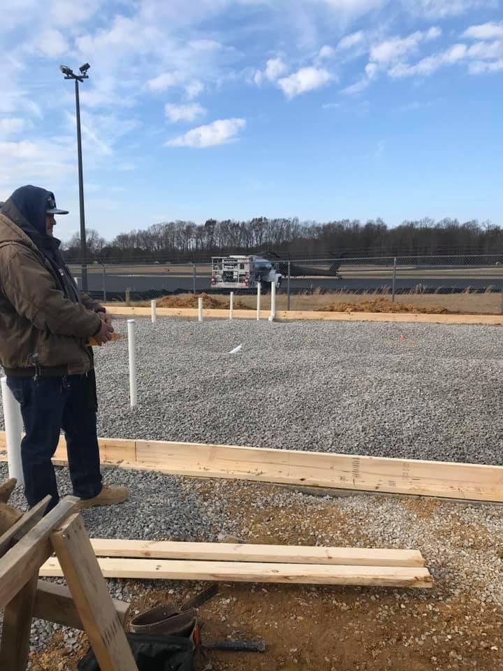 Person flying a drone at a construction site with gravel, lumber, and a partly cloudy sky