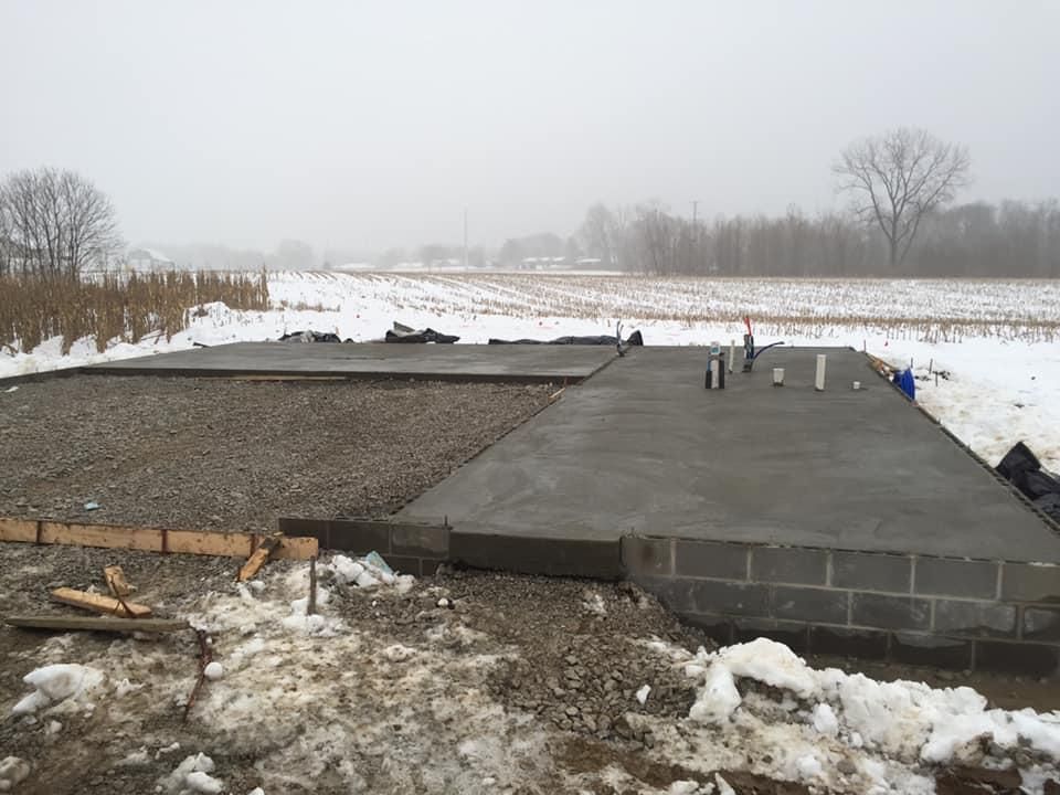 Concrete foundation in snowy rural field under overcast sky