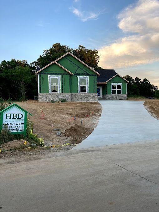 Two green houses with a curved concrete driveway at dusk, and an HBD sign by the roadside