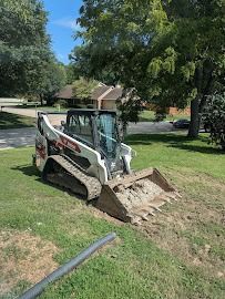 White skid-steer loader digging a grassy yard near a house and trees