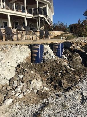 Collapsed hillside beside house with exposed blue foundation support tubes and debris under a deck