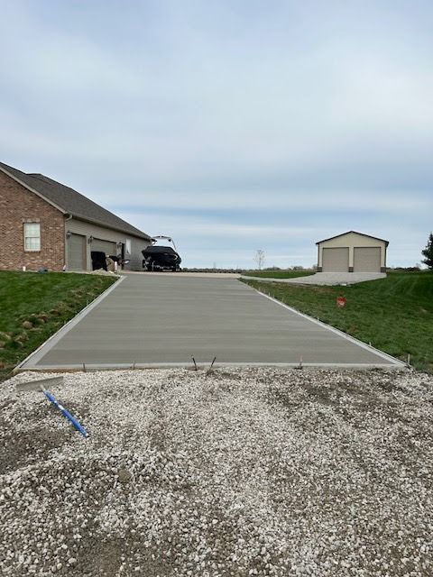 Concrete driveway leading up to a brick house and detached garage under a cloudy sky