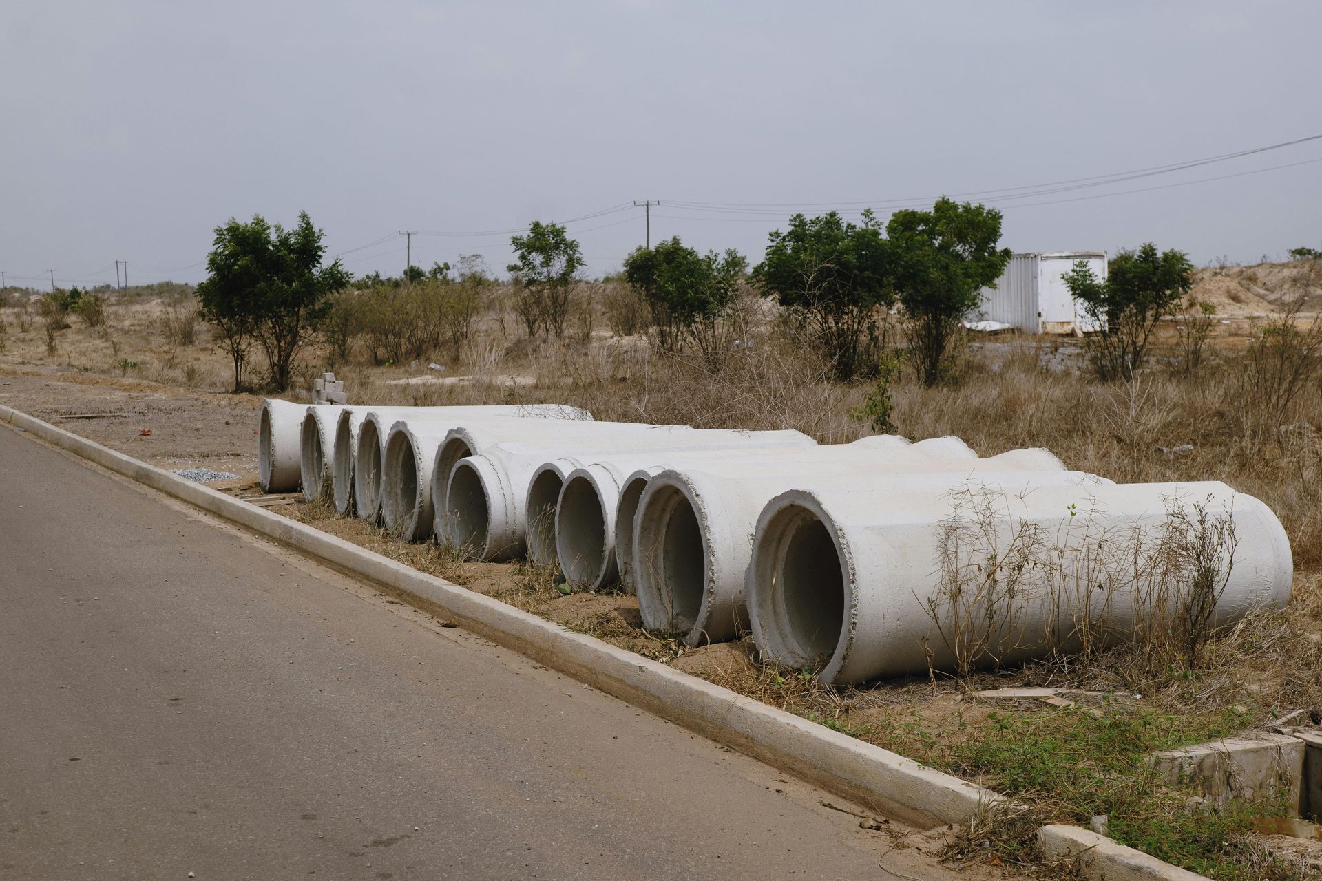Large concrete drainage pipes lined along a roadside in a dry, grassy area