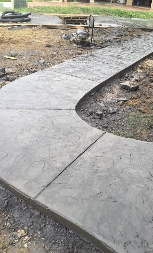 Curved concrete walkway under construction beside muddy ground and a small central fountain.