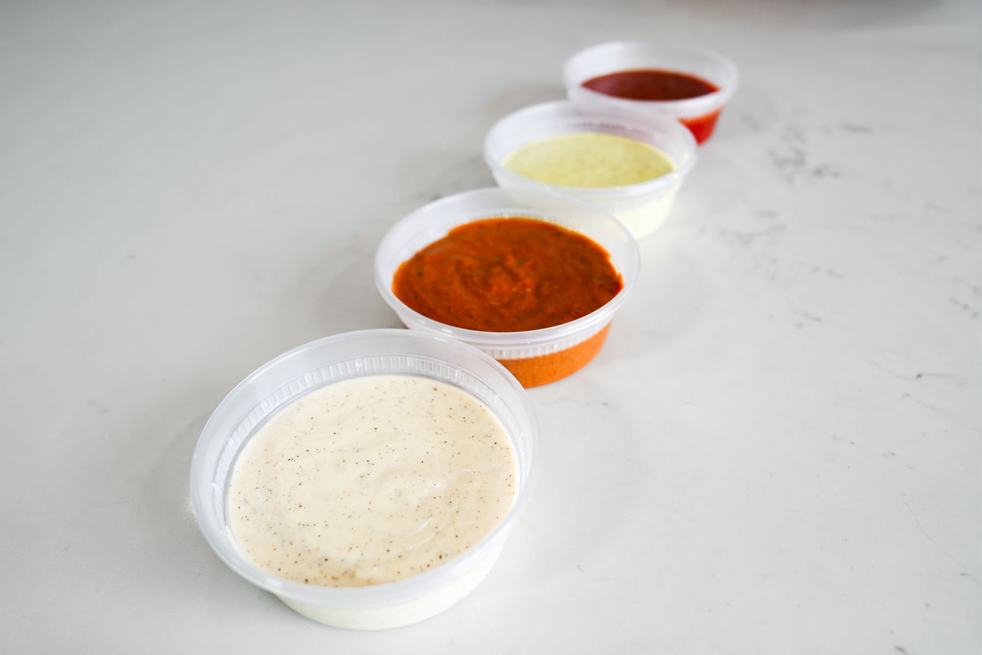 Four small bowls of colorful sauces on a white surface, arranged diagonally in a row.