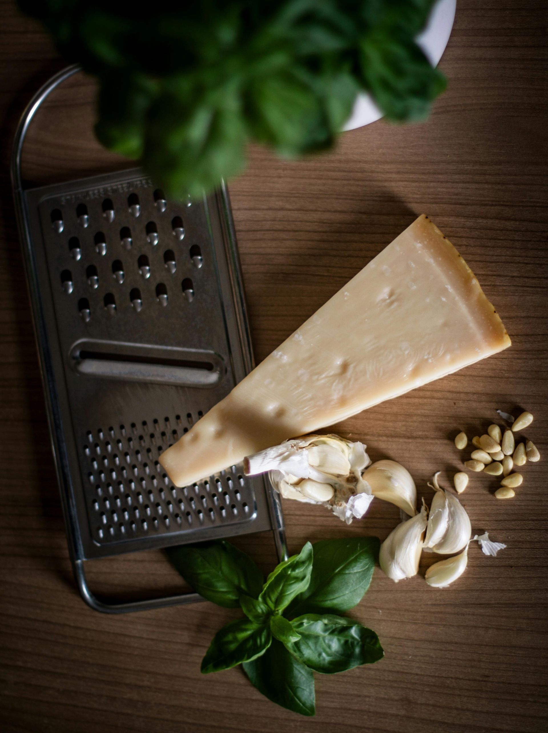 Cheese wedge, grater, garlic, basil, and peppercorns on a wooden table