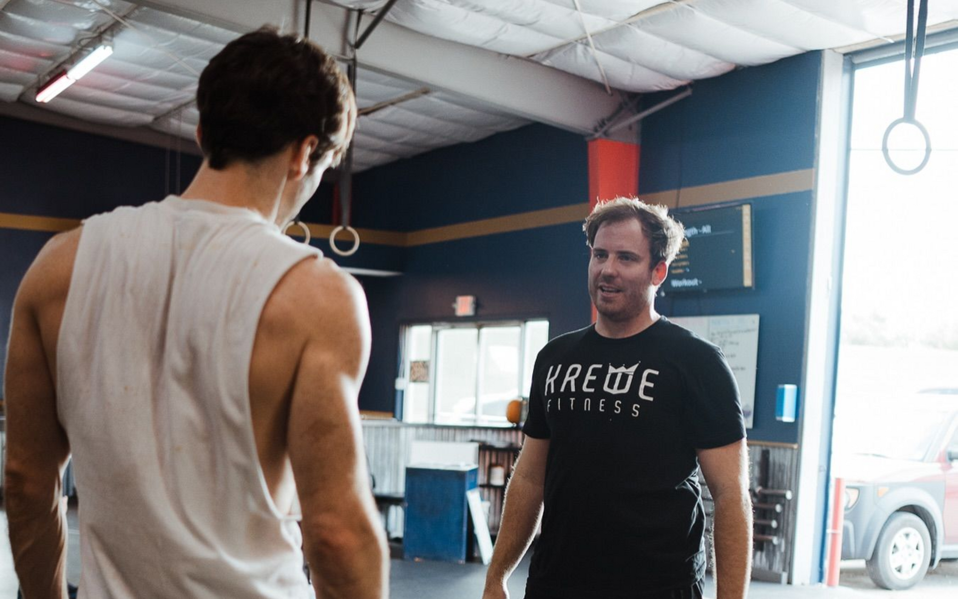 Two individuals face each other in a gym in New Orleans, one wearing a white tank top and the other a black t-shirt.