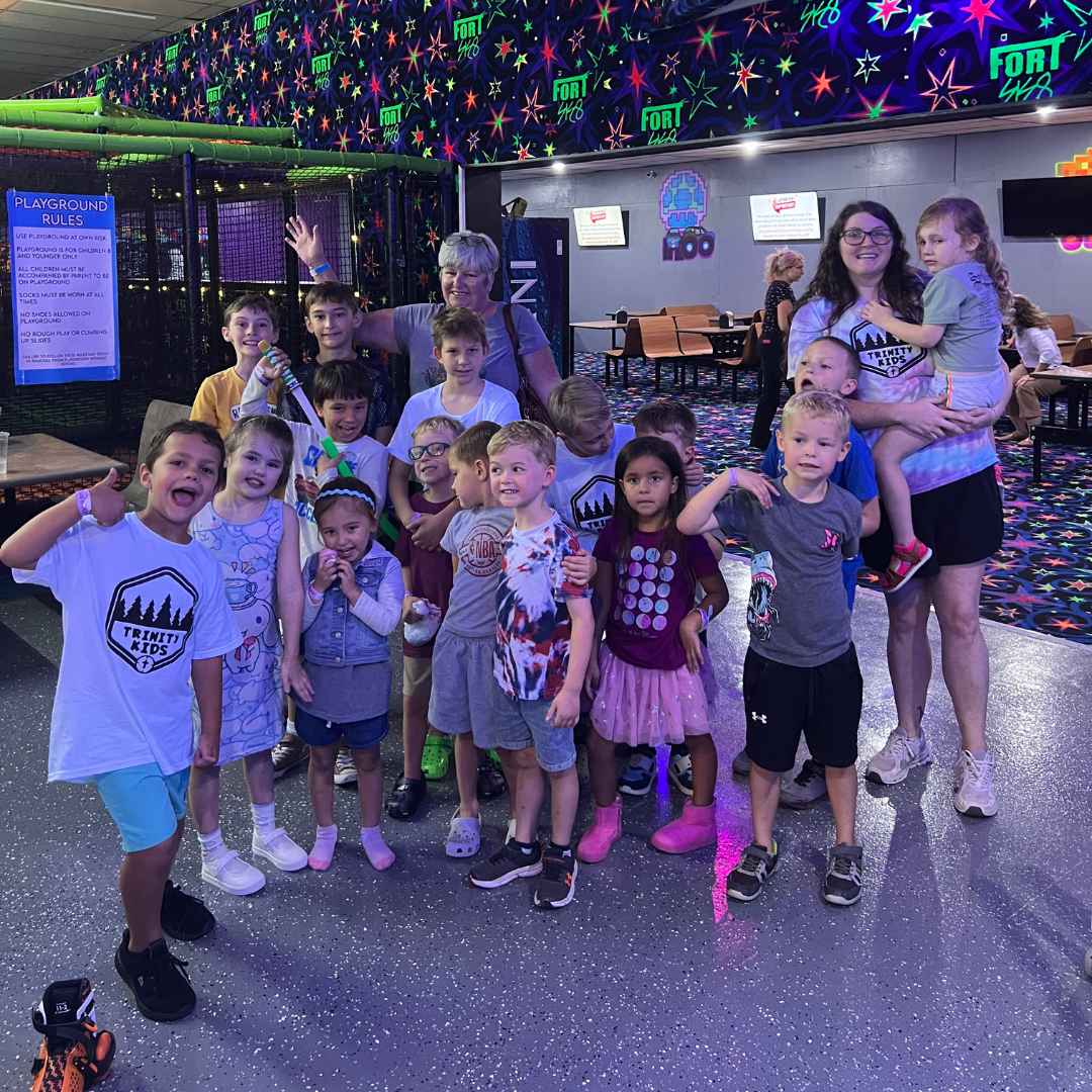 Group of children posing together in a roller rink with colorful neon lights and glittery floor.