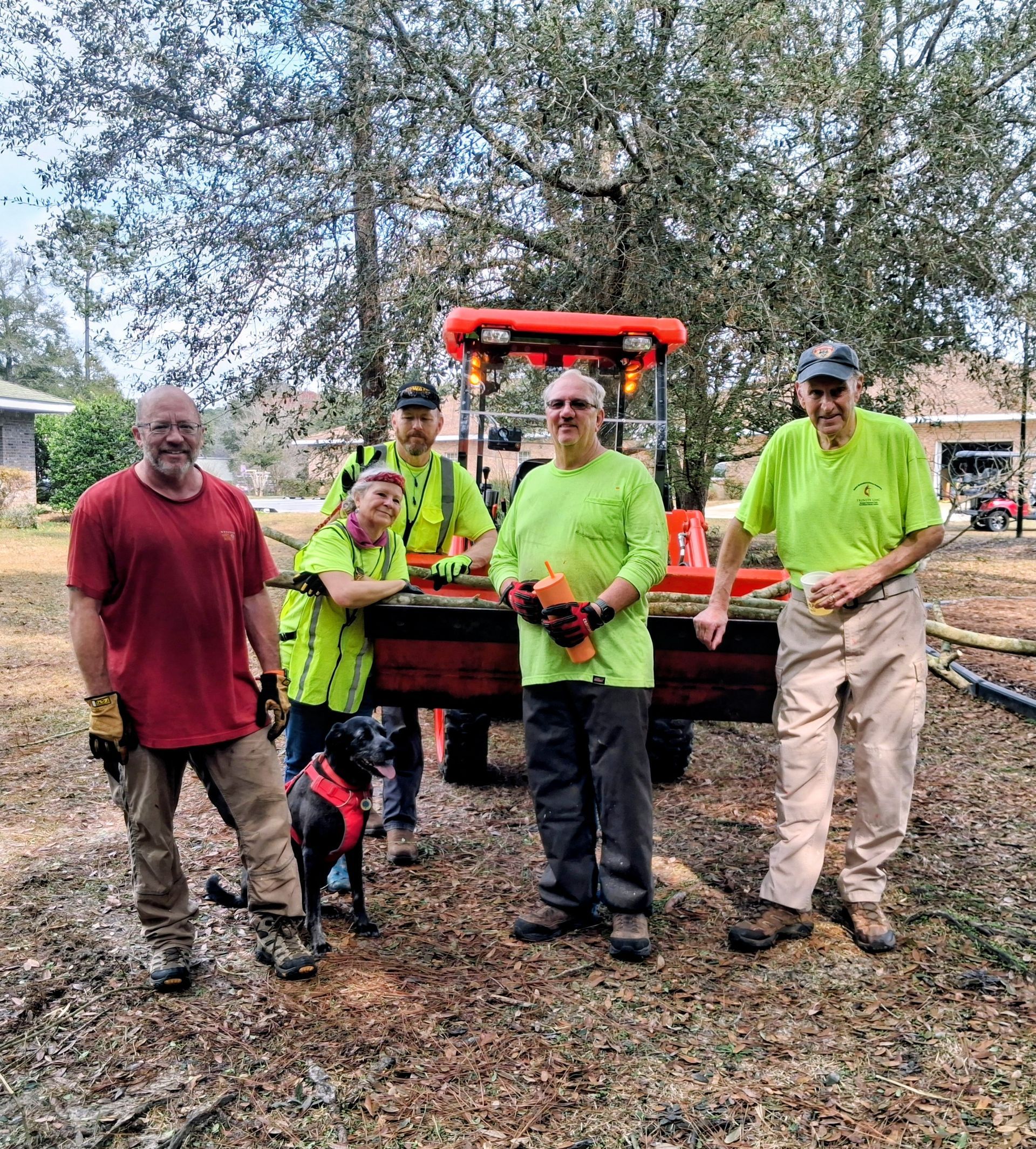 Five workers in neon shirts posing in front of an orange utility vehicle in a wooded area.