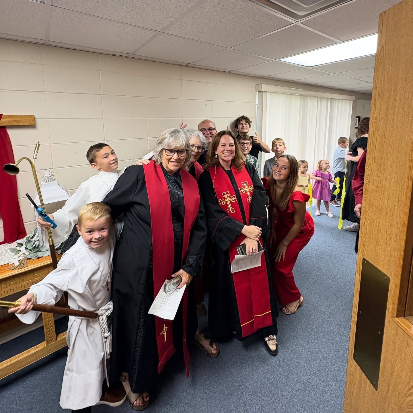 Group in red-and-black robes and costumes walking together indoors, smiling in a hallway.