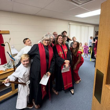 People in robes posing in a hallway, smiling near a child dressed as acolytes