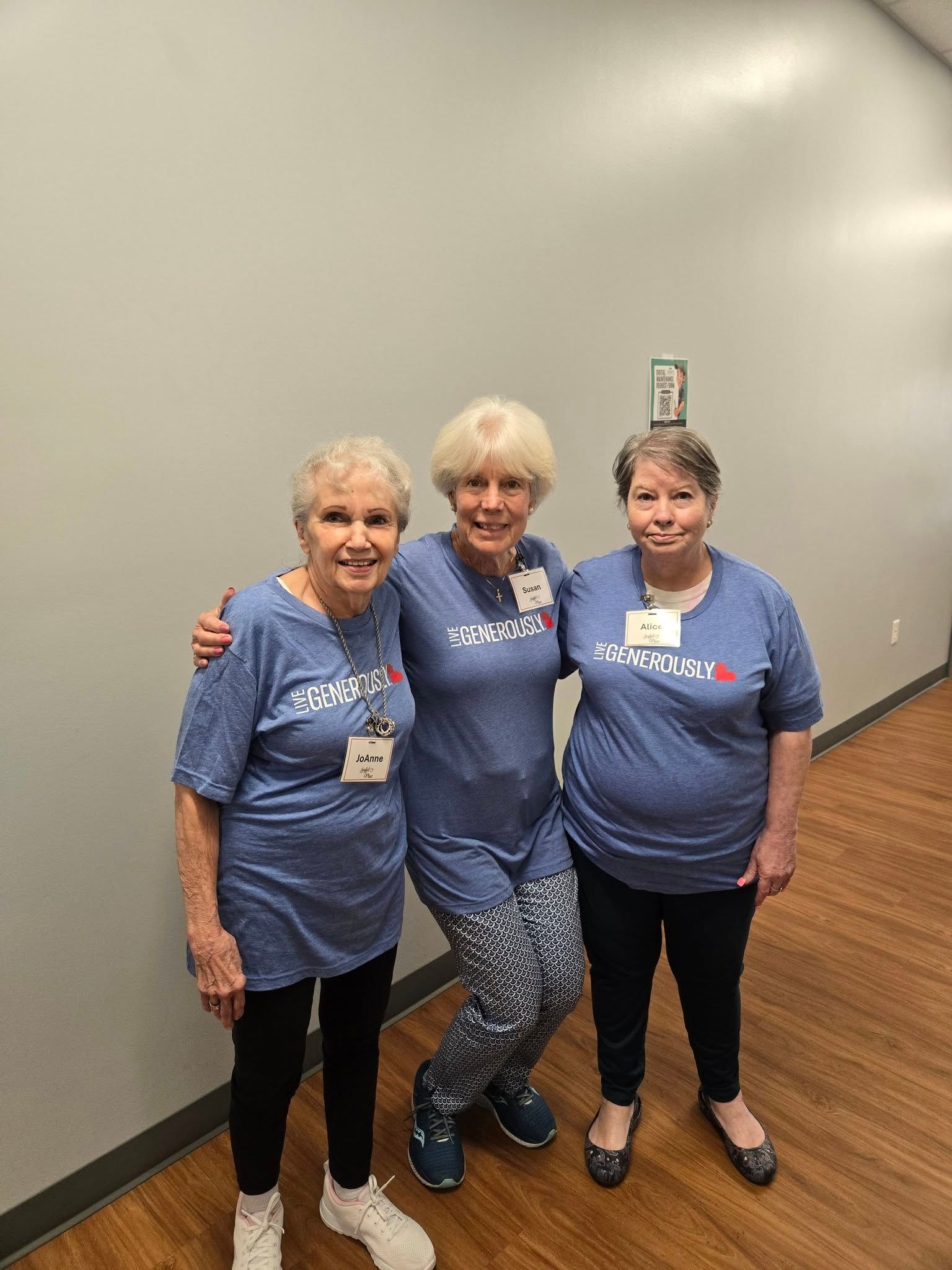 Three people in blue shirts pose together in a hallway, smiling at the camera.
