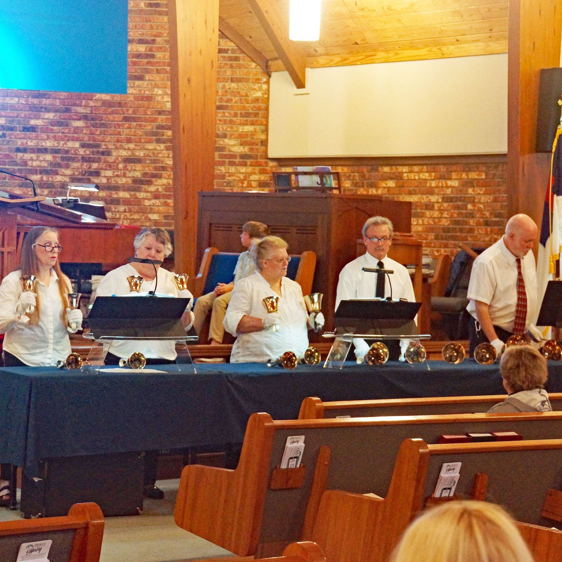 Choir members seated at a table with microphones in a church hall, preparing to sing.