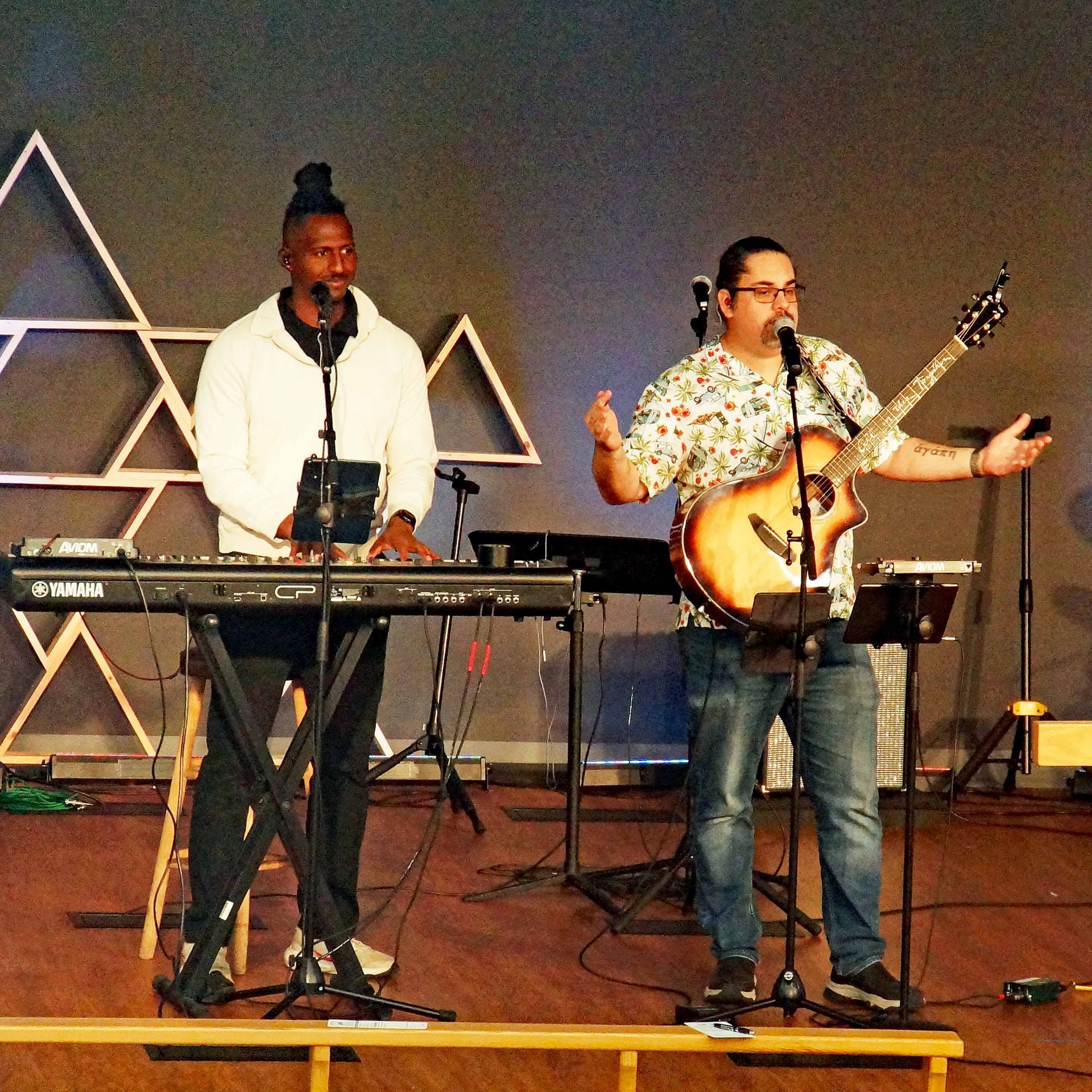 Two musicians perform on stage, one at a keyboard and one singing with a guitar.