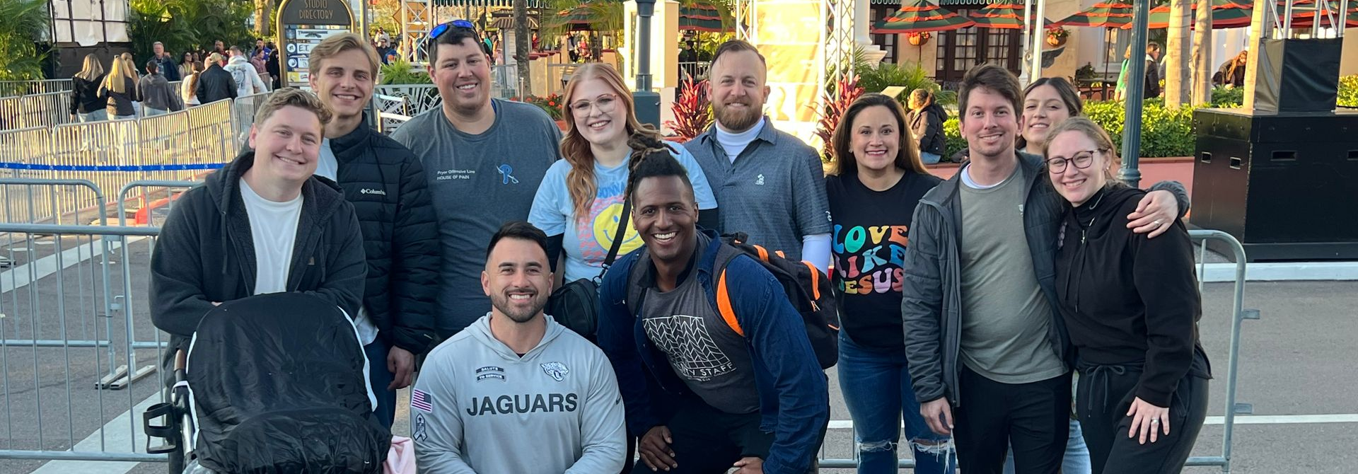 Group of people posing outdoors in front of a fountain, smiling in casual winter clothing.
