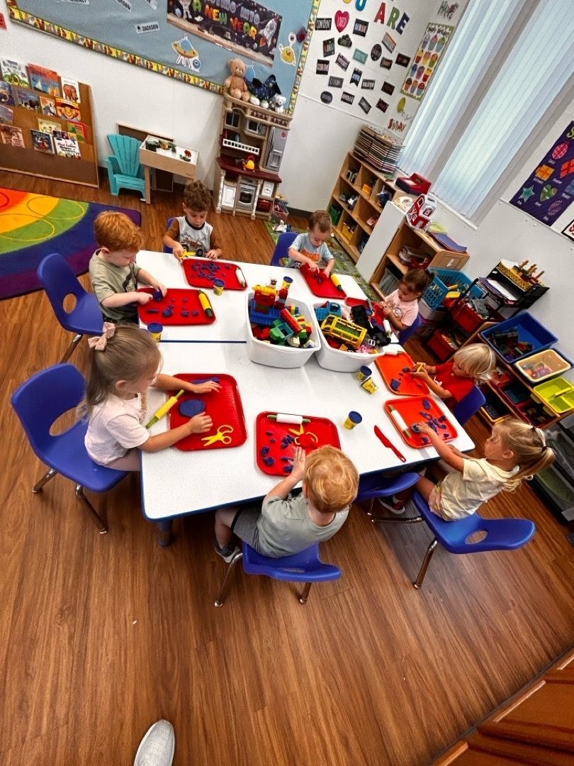 Children seated around a table making crafts with red trays in a colorful classroom