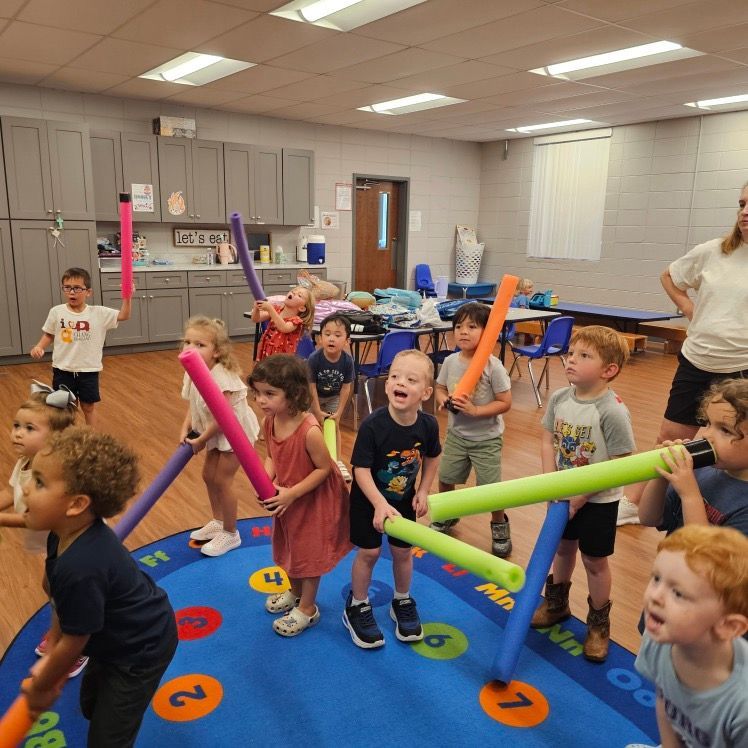 Children holding colorful foam tubes during an indoor group activity in a classroom or gymnasium