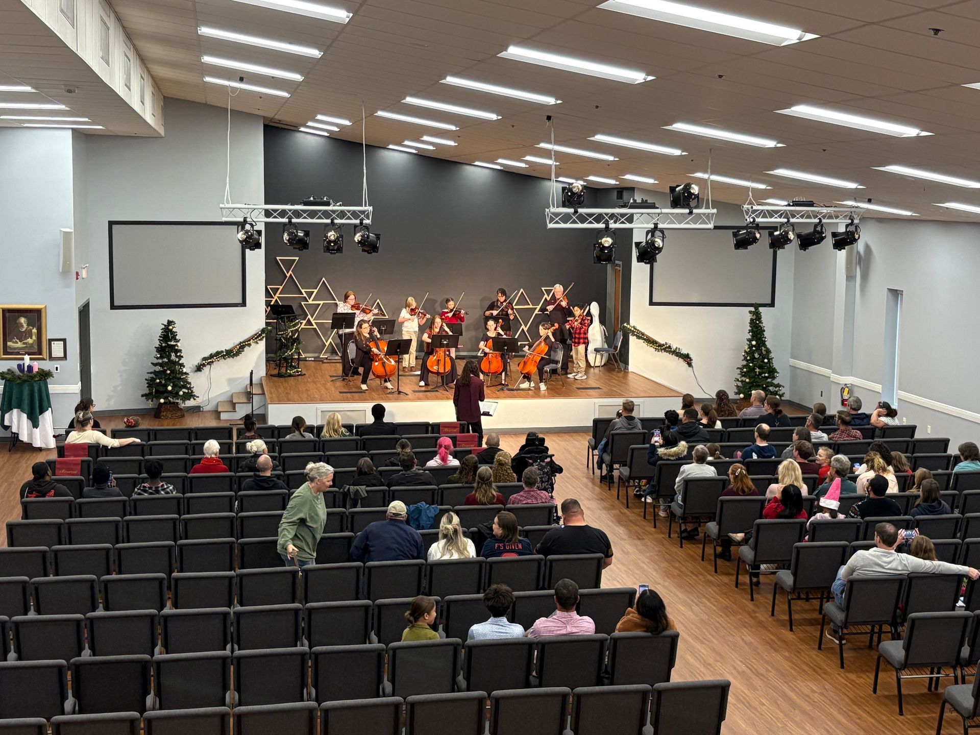 Concert in a large hall with an audience seated before a stage orchestra under bright lights
